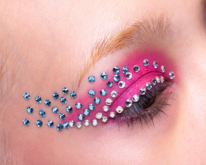 open eye with white and blue crystals and pink eyeshadow closeup