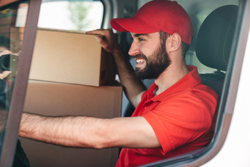 Canvas Print - Image of happy young delivery man smiling and driving van