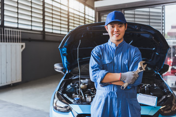 Happy car mechanic inspection technician holding wrench and smiling to camera after fixing customer car claim in service maintenance insurance of car engine. Transportation automotive industry concept