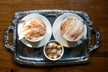 Silver tray with two capuccinos and sugar