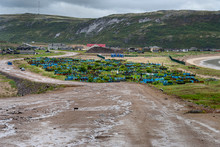 Russia, Arctic, Kola Peninsula, Barents Sea, Teriberka: Long Road Down To The Oldest Part Of Russian Settlement Small Fishing Village With Cemetery, Old Buildings, Mountains, Cloudy Sky. Jul 17, 2019