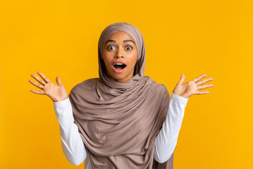 Wall Mural - Surprised afro muslim woman in headscarf raising hands in shock