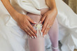 In the morning, the bride in stockings and a white wedding dress wears a garter on her leg, the bride is holding her hands for the garter.