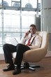 © moodboard - Businessman in arm chair working on laptop on the phone
