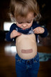 © Cavan Images - Young toddler girl looking at bandaid on belly
