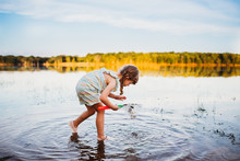 Young Girl Bending Down To See Fish In Water At The Lake