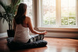 © Cavan Images - Woman sitting on the floor indoors meditating in front of windows.