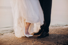 The View Of The Newlyweds Legs And Shoes Standing On The Beach.