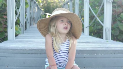 stylish little girl in a straw hat sits alone in the park. face close-up