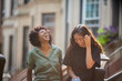 © Cavan for Adobe - Female friends laughing while standing against houses in city