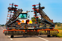A Farmer Is Seen Driving A Large Industrial Tractor From Behind, With Extending Rotary Tillage And Plow Attachment For The Management Of Farmland