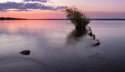 old fishing pier with tree at the end glass like water during colorful sky at sunrise or sunset.  Presque Isle Bay in Erie, Pennsylvania