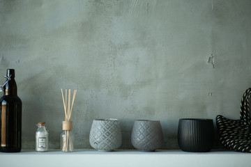 Dark minimalistic bathroom decor - dark glass vase, wood box, towel, products and accessories for care face skin on white wood table and gray wall, closeup