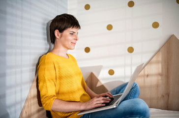 Wall Mural - Young woman with laptop sitting on bed in bedroom indoors at home.