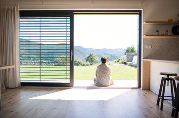 Rear view of young woman sitting by patio door at home. Copy space.