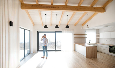 Wall Mural - Mature man standing in new house, using smartphone.