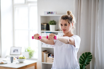 Young woman with dumbbells doing exercise in bedroom indoors at home.