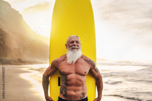 Fotomural Happy fit senior having fun surfing at sunset time - Sporty bearded man training