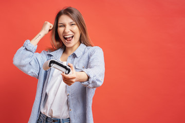 Wall Mural - Competitive girl celebrates winning holding game joystick controller on red background.