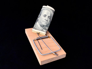 Dollars in a mousetrap on a black background. Wooden trap with bait and mechanism for rats and mice. Concept: happiness is not money, greed