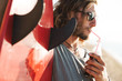 © Drobot Dean - Photo of handsome bearded man drinking soda and holding surfboard