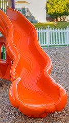 Wall Mural - Vertical Close up of bright and shiny orange slide at a park with childrens playground