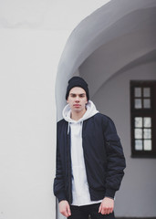 Wall Mural - tough man in a black hat and jacket stands outside a white old building.