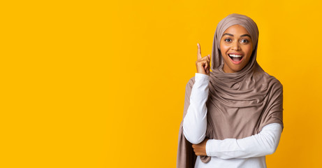 Wall Mural - Overjoyed black muslim girl in hijab having idea, pointing finger up