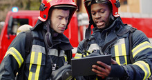 Portrait Of Two Firefighters In Fire Fighting Operation, Fireman In Protective Clothing And Helmet Using Tablet Computer In Action Fighting.