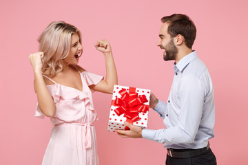 Wall Mural - Couple two guy girl in party outfit celebrating isolated on pastel pink background. Valentine's Day Women's Day birthday holiday concept. Hold present box with gift ribbon bow, doing winner gesture.