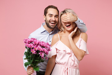 Wall Mural - Laughing young couple two guy girl in party outfit celebrating isolated on pastel pink background. Valentine's Day Women's Day birthday holiday concept. Hold bouquet of flowers, cover eyes with hand.