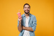 © ViDi Studio - Funny young man in casual blue shirt posing isolated on yellow orange wall background, studio portrait. People sincere emotions lifestyle concept. Mock up copy space. Hold in hand cup of soda or cola.