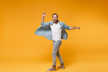 Wall Mural - Laughing young bearded man in casual blue shirt posing isolated on yellow orange background studio portrait. People sincere emotions lifestyle concept. Mock up copy space. Spreading rising hands up.