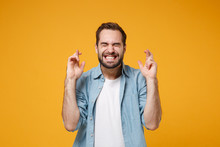 Young Bearded Man In Blue Shirt Posing Isolated On Yellow Orange Background. People Lifestyle Concept. Mock Up Copy Space. Waiting For Special Moment Keeping Fingers Crossed, Eyes Closed, Making Wish.