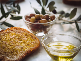 slices of bread with extra virgin oil near to glass bowls filled oil and olives. Olive leaves on background. Healthy food, healthy diet, traditional mediterranean product 2