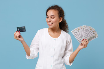 Wall Mural - Pretty african american doctor woman isolated on blue background. Female doctor in medical gown hold fan of cash dollar money, credit card. Healthcare personnel medicine concept. Mock up copy space.