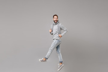 Cheerful young bearded man in gray sweater scarf posing isolated on grey background studio portrait. Healthy fashion lifestyle people sincere emotions cold season concept. Mock up copy space. Jumping.