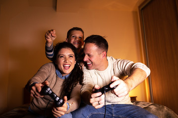 Parents with the children sitting at home on a pleasant evening and playing games on console. They challenge each other to win.		