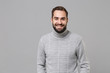 Smiling young bearded man in gray sweater posing isolated on grey wall background, studio portrait. Healthy fashion lifestyle, people emotions cold season concept. Mock up copy space. Looking camera.