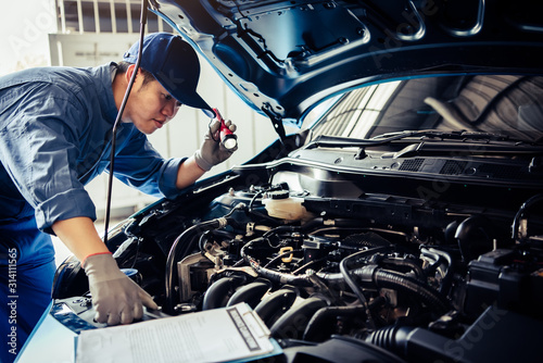 Cuadros en Lienzo Car mechanic technician holding flashlight checking engine with checklist clipboard to maintenance vehicle by customer claim order in auto repair shop garage repair service