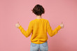 Back rear view of young brunette woman girl in yellow sweater posing isolated on pink wall background studio portrait. People sincere emotions lifestyle concept. Mock up copy space. Showing thumbs up.