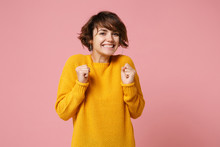 Smiling Joyful Young Brunette Woman Girl In Yellow Sweater Posing Isolated On Pastel Pink Background Studio Portrait. People Sincere Emotions Lifestyle Concept. Mock Up Copy Space. Clenching Fists.