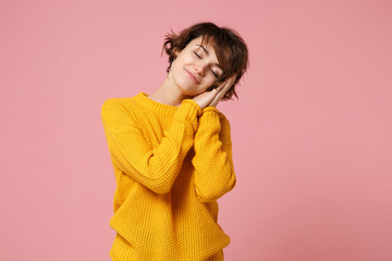 Wall Mural - Relaxed young brunette woman girl in yellow sweater posing isolated on pastel pink wall background studio portrait. People lifestyle concept. Mock up copy space. Sleep with folded hands under cheek.