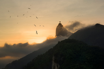 Wall Mural - sunset in rio de janeiro - frigate birds in sky with silhouette of christ redeemer rising from fog i