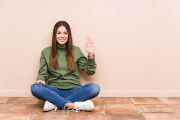 Young caucasian woman sitting on the floor isolated smiling cheerful showing number five with fingers.