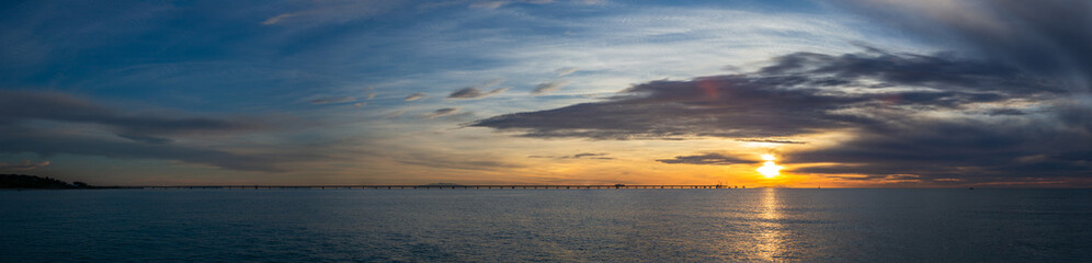 A pier on the Mediterranean Sea in Tuscany at sunset with an island and a sailboat in the background