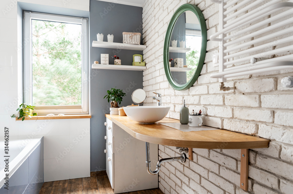 Bright interior of bathroom with window, wooden furniture and counter, round mirror and white brick wall. Simple and stylish design in scandinavian style. - obrazy, fototapety, plakaty 