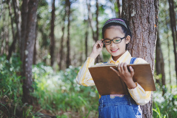 Canvas Print - Cute little girl with glasses reading book in garden