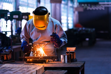 Industrial welder is welding metal part in the factory.