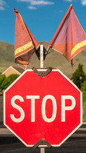 Vertical Selective Focus Of Traffic Stop Sign With Two Red Flags Against Road And Houses